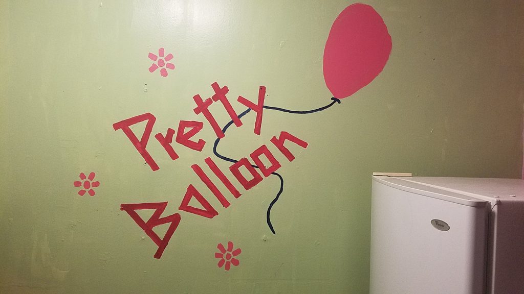A red balloon on a green background, surrounded by simple flowers, with the string behind the words "Pretty Balloon" also in red.